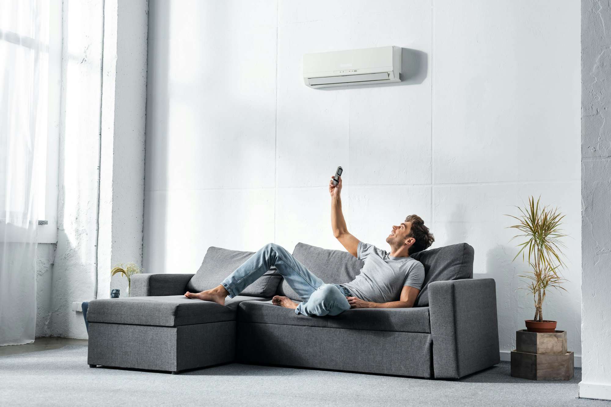 handsome man lying on sofa and switching on air conditioner